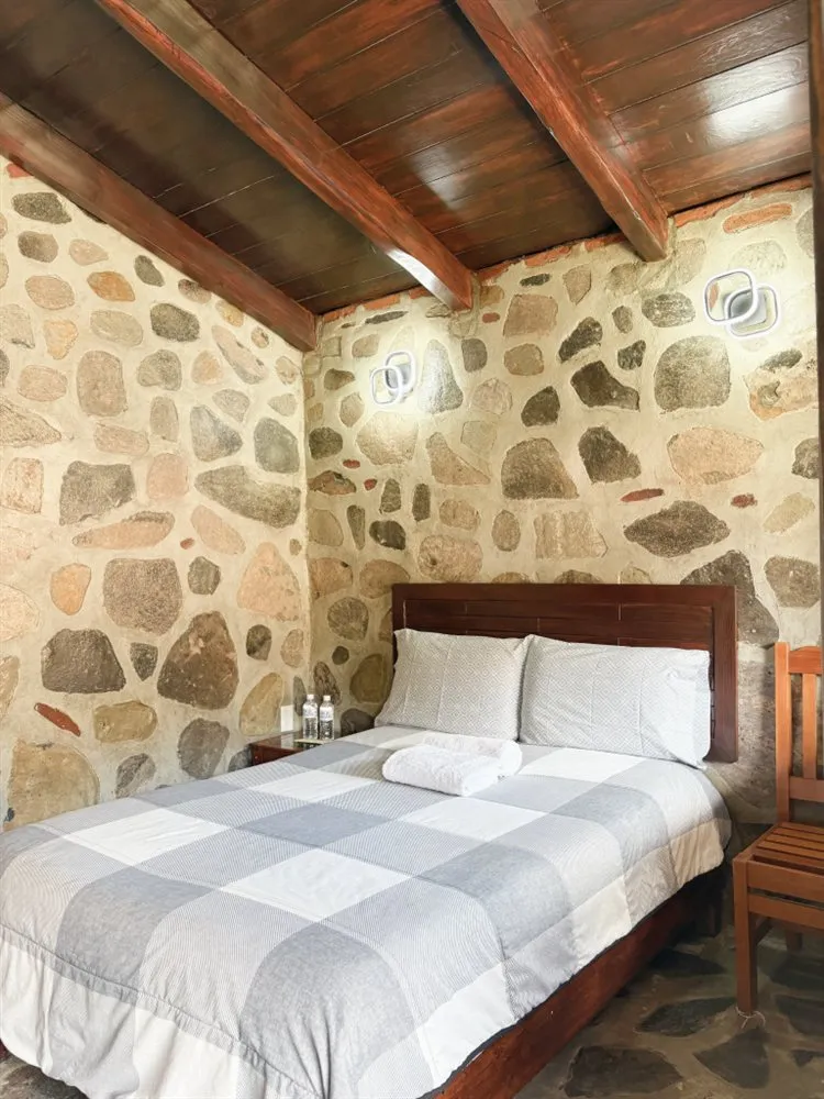 Interior de cabaña de piedra con cama y techo de madera